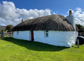 Exterior of a restored Scottish croft with stone walls thatched roof in a remote location on Skye