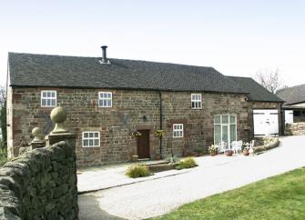 Exterior of a large tone-built barn conversion overlooking a driveway and lawn in Ipstones