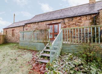 Single-storey brick-built barn conversion forming a holiday cottage with a long deck and lawned garden with a light sprinkling of winter snow. overlooking a