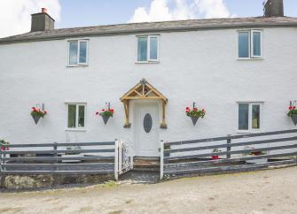 Front exterior of a double-fronted2-storey  Welsh holiday cottage with wall-mounted flowerpots and a wooden fence.