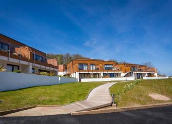 A row of 2-storey seaside holiday apartments in Brixham with seaward-facing balconies overlooking a grassy slope towards a beach below