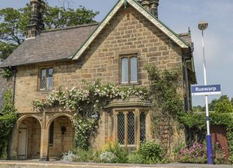 Exterior of a stone-built station-master's house overlooking a platform of a steam railway.