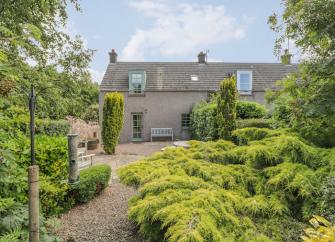 A small holiday cottage in St. Abbs sits behing a flourishing garden of small trees,sshrubs and a winding garden path.