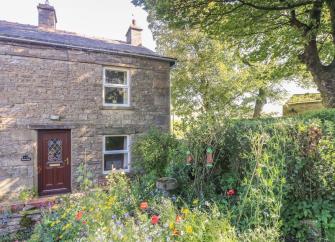 A stone built country cottage in the Yorkshire Dales overlooks a mature garden with flowering poppie.