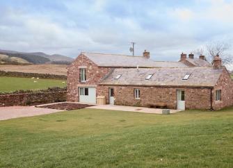 Exterior of a Cumbriain stone. barn conversion near surrounded by fields.