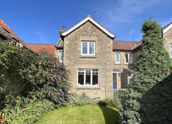 Exterior of a North Yorkshire holiday cottage overlooking a lawn lined by trees.