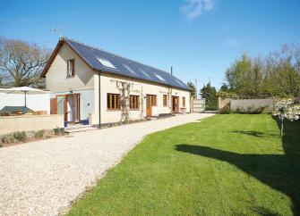 Exterior of a long house with velux windows having a wide drive and lawned gardens bordered by hedges and trees in the Devon countryside.
