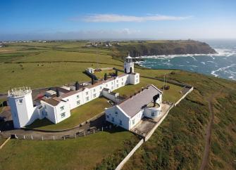 Aerial view of a Lighthouse and crew buildings atop cliffs overlooking the sea at Lizard Point in Cornwall.