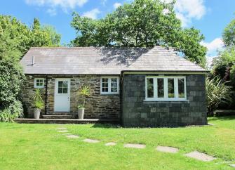 Granite-built exterior of a single storey Cornish holiday home surrounded by lawns.ottage