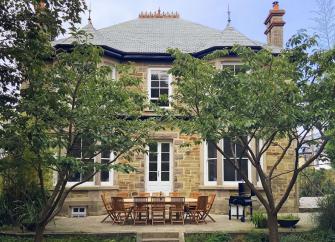 Double-fronted stone exterior of a Cornish cottage with bay windows and a terrace for outdoor dining.