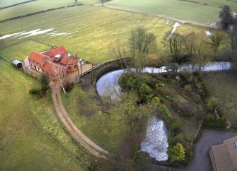 A farmhouse and attached barns in open countryside overlook a bend in a river