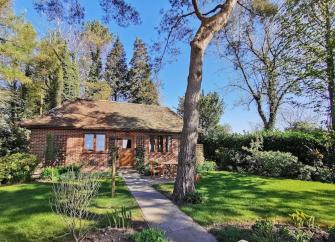 Exterior of a brick-built Dorset bungalow surrounded by lawns, shrubs and mature trees.