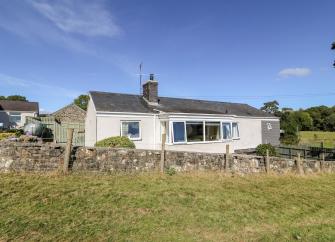 Exterior of a modern bungalowsurrounded by a low stone wall and surrounded by open fields.