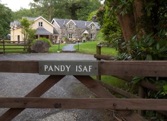 Behnd a wooden 5-bar gate astone-built Gwynedd holiday cottage with twin gables overlooks a large lawn