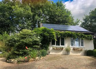 Exterior of a single-storey, vine-dlad, one bedroom holiday bungalow near Bude overlooked by mature trees.