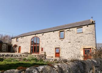 Exterior of a long, stone-built barn conversion in Priestcliffe, overlooking a courtyard and a walled garden.