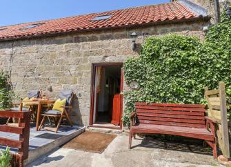 A cosy stone-built cottage in Danby on a sunny day with a garden bench and patio.