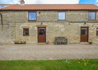 2-storey exterior of. stone-built barn conversion overlooking a paved terrace and a lawn