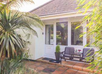 Front entrance and patio to  Praa-Sands holiday cottage fronted by a palm tree and shrubs.