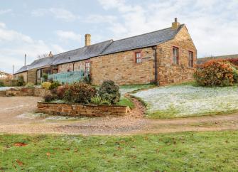 A single-storey, stone-built barn conversion in Cumbria with parking spaces and lawns.
