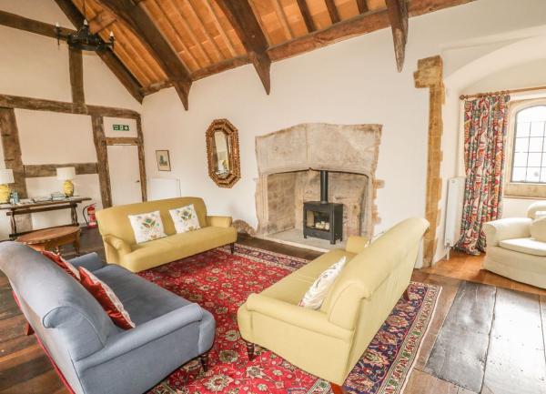 Lounge with 3 sofas, inglenook fireplace containing a wood burner andardhed oak beams overhead.