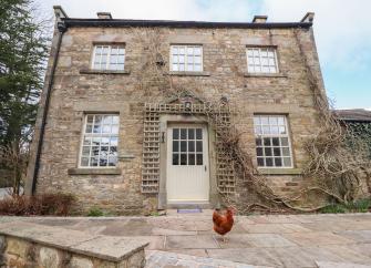 A double-fronted exterior of a converted coach house with large quartered windows overlooking a flagstoned courtyard.