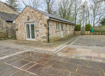 Exterior of a single storey stoe cottage, backed by trees and overlooking a large flagstoned courtyard.