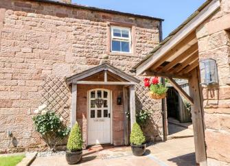 Entrance to a stone-built Cumbrian coottage with a porch and small lawn.