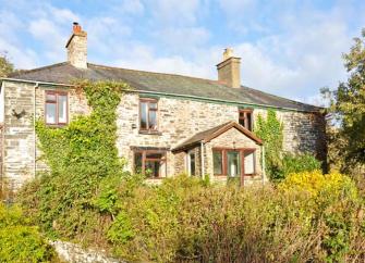 Frontage of a creeper-clad stone farmhouse overlooking mature gardens.