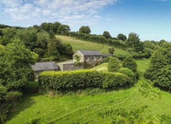 A log cabin nestles against a hillside surrounded by trees and bushes on Exmoor.