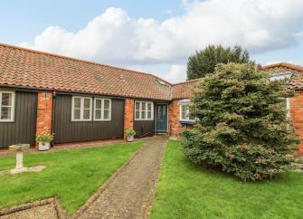 A single-storey wooden brick path crosses a lawn to the front door of wooden barn conversion 