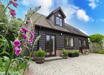 Exterior of a 2-storey wooden cottage overlooking a large drive bordered by flowers.