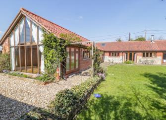 L-shaped exterior of a barn conversion with a gable end of wood-framed glass windows overlooking a large lawn. 