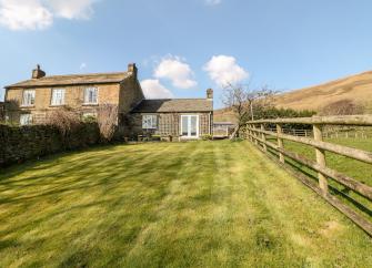 A large cottage with a ground floor extension is surrounded by open fields and moorland.