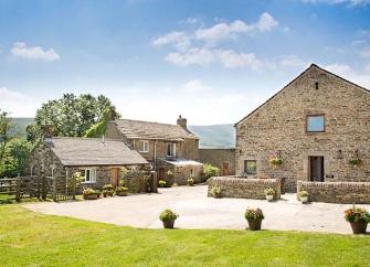 A 2-storey barconversion with a low stone wall overlooks a paved drive and a spacious lawn.