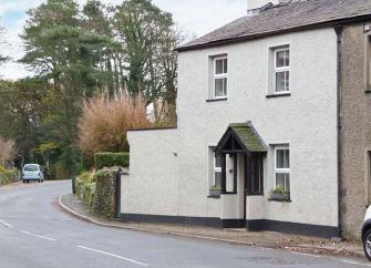 A white-rendered cottage with a small porch overlooks a village street.