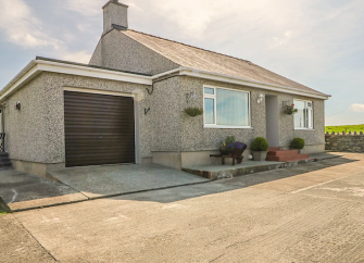 A countryside holiday bungalow in Anglesey with a garage and surrounded by fields.