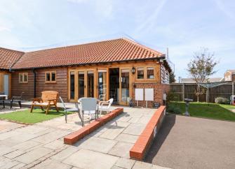 Exterior of a single-storey norfolk holiday cottage with outdoor seating and block-paved off-road parking.