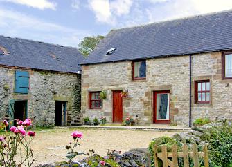 A stone-built cottage overlooks a cobbled courtyard bordered by a low stone wall.