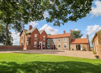 Exterior of a large, L-shaped brick East Yorkshire farmhouse overlooking a spacious courtyard and lawn.