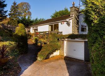 A modern house with a vine covered 1st floor balcony overlooks a shrub-filled front garden.