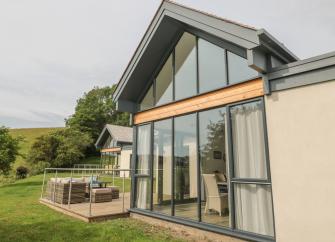 A gable end with floor to roof windows overlooks a lawn with a deck.