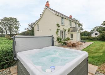 A hot tub bubbles away i in front of an elegant Pembrokeshire holiday cottage surrounded by  a patio and lawns.