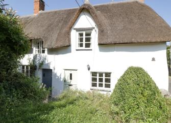A thatched holiday cottage in Kilve overlooks a shrub-filled garden on the Somerset coast.