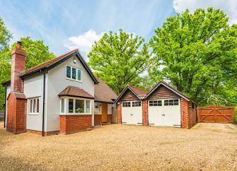 Exterior of a New Forest holiday cottage with a brick chimney stack, twin garages and backed by woodland trees.