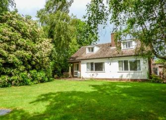 A Horning holiday cottage overlooks a large lawn shaded by tall trees.