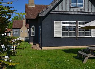 A two-storey Essex holiday cottage overlooking a lawn with a parasol on Osea Island