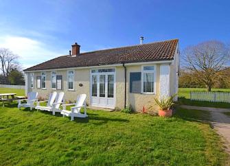 Exterior of an Osea Island holiday bungalow surrounded by lawns containing sun loungers and a picnic table