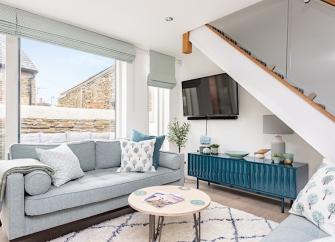 Carpeted lounge area with large windows in a Kingsbridge holiday cottage with sofa, large cupboard and coffee table