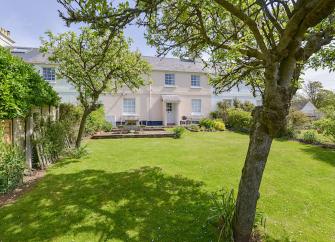 A double-fronted Hope Cove holiday cottage overlooks a large lawn.